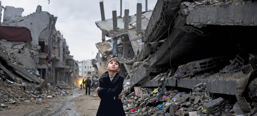 A Palestinian boy looks up during a rain storm while walking through a neighbourhood destroyed during the 50 day conflict between Israel and Hamas, in the Shejaiya neighbourhood of Gaza City on October 19, 2014. United Nations chief Ban Ki-moon said that the promised aid funds to rebuild would go towards the 