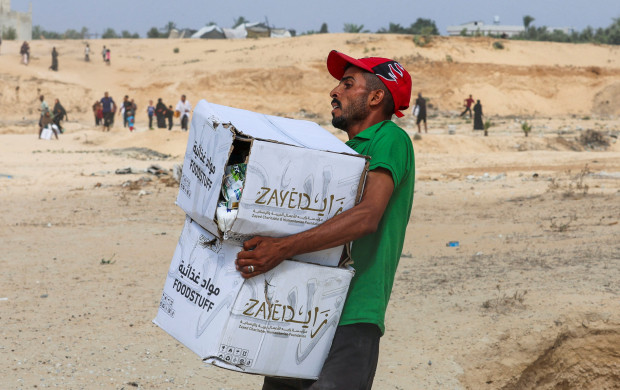 <p>A Palestinian man carries food items collected from aid packages dropped from an airplane, amid a hunger crisis, in Deir Al-Balah, in the central Gaza Strip, August 12, 2025. REUTERS/Ramadan Abed</p>